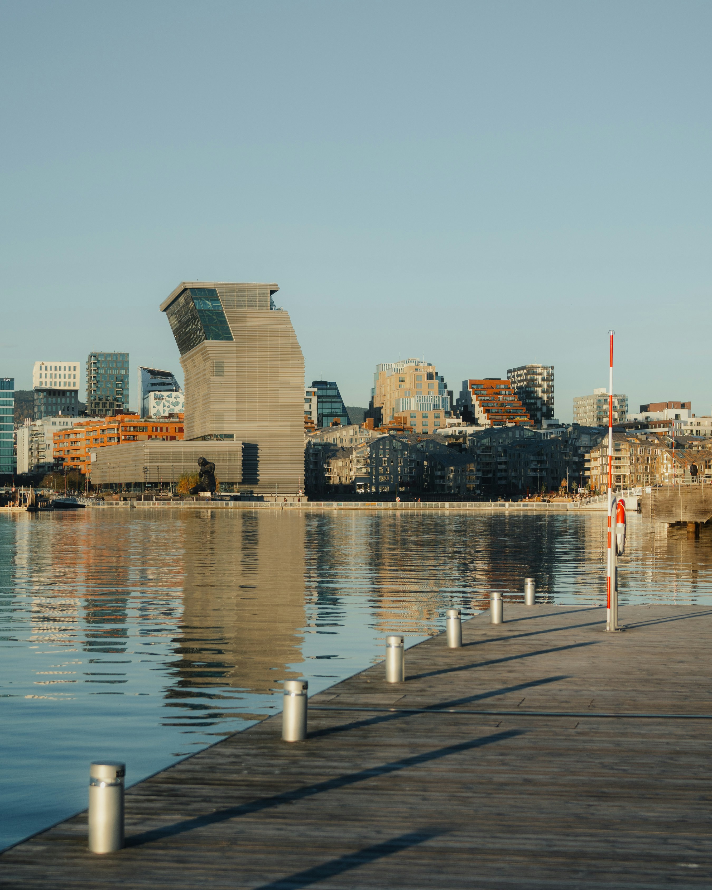 Modern buildings reflected in the water by a pier.