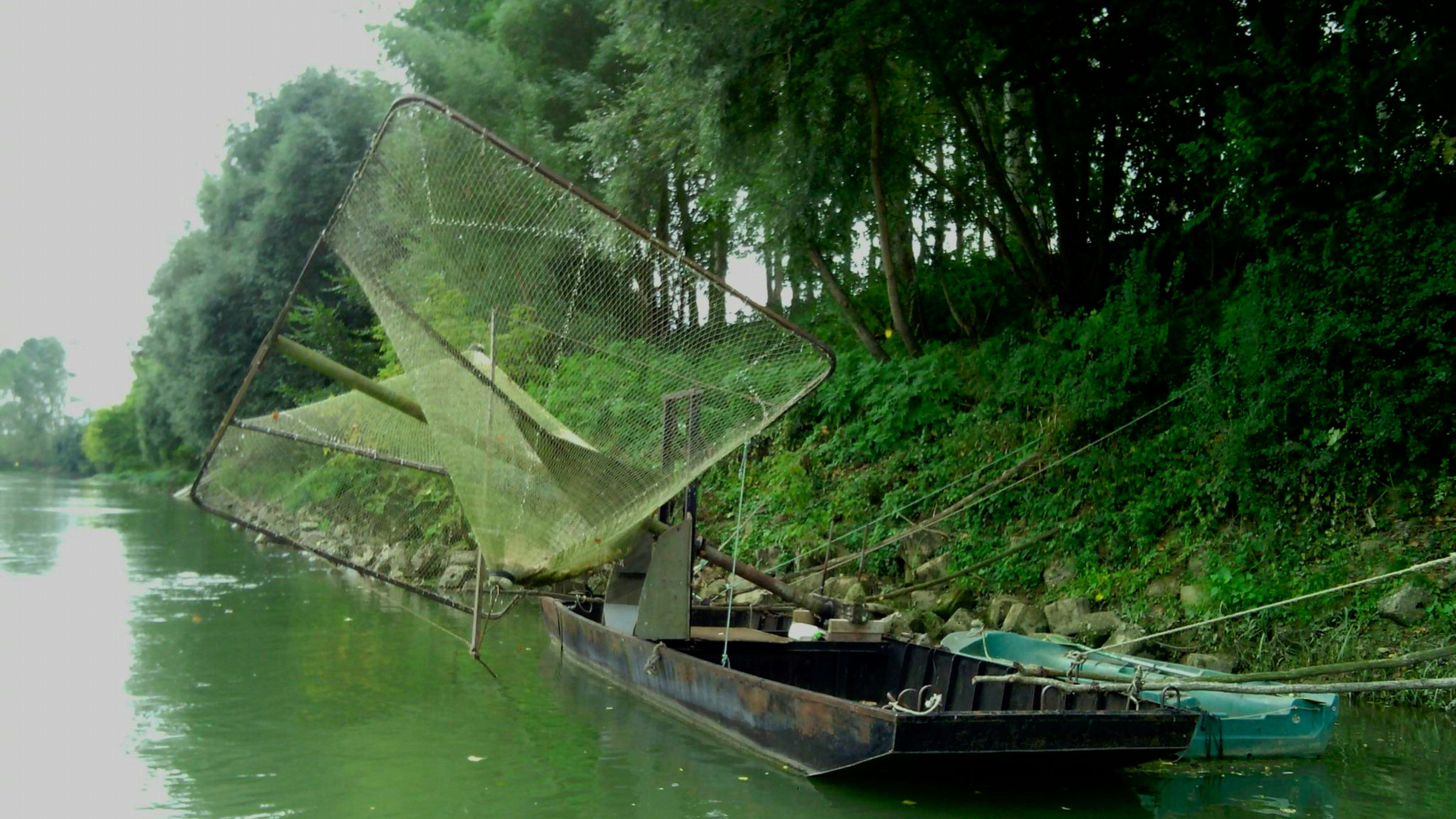 Fishing boat with large nets on a calm river.