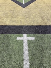 White cross marking on green turf field with yellow lines