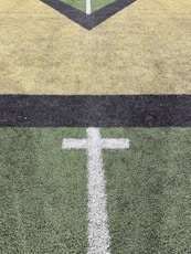 White cross marking on green turf field with yellow lines