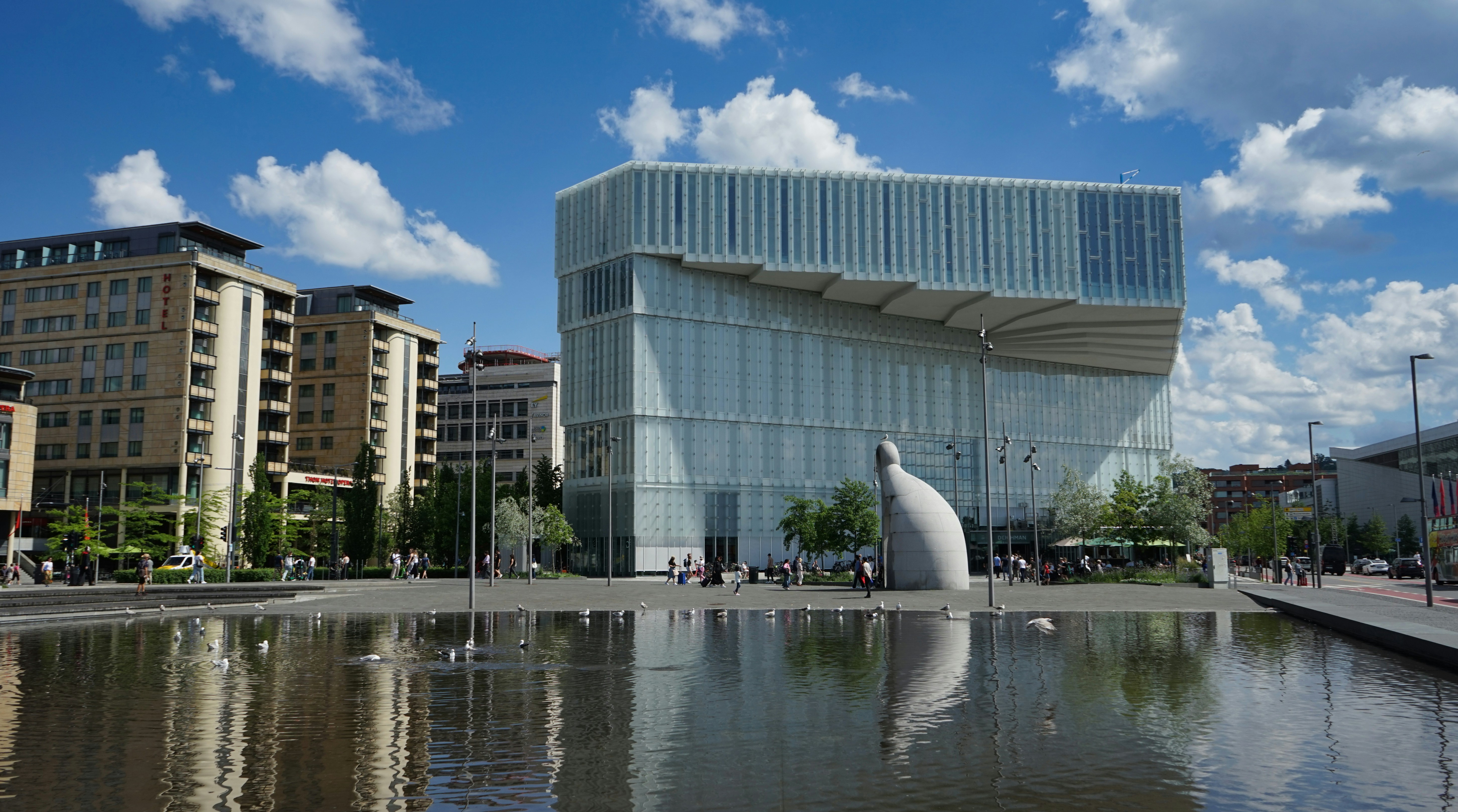 Modern glass building reflected in water under a blue sky.