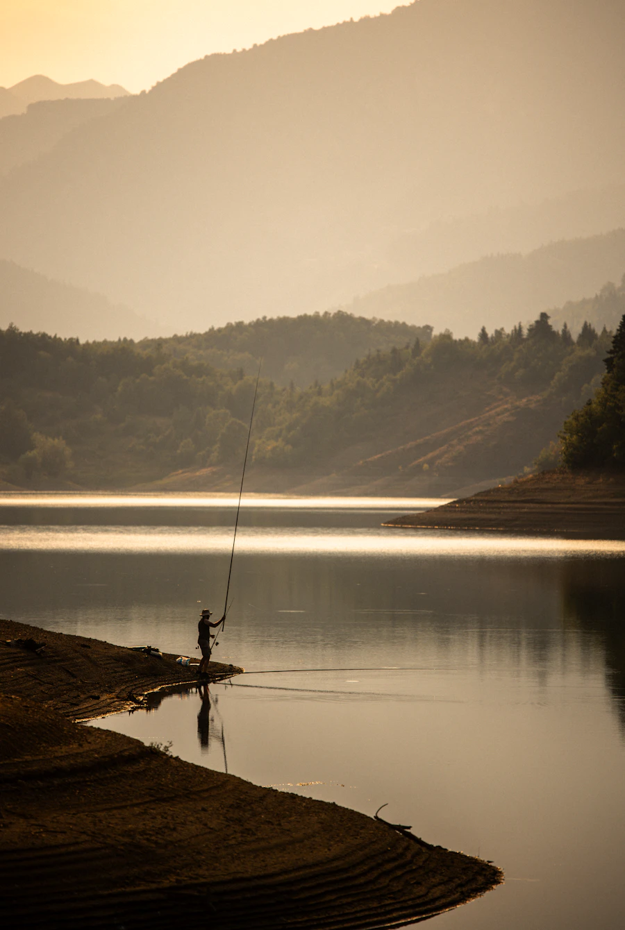 Fisherman casting line on tranquil lake at sunset