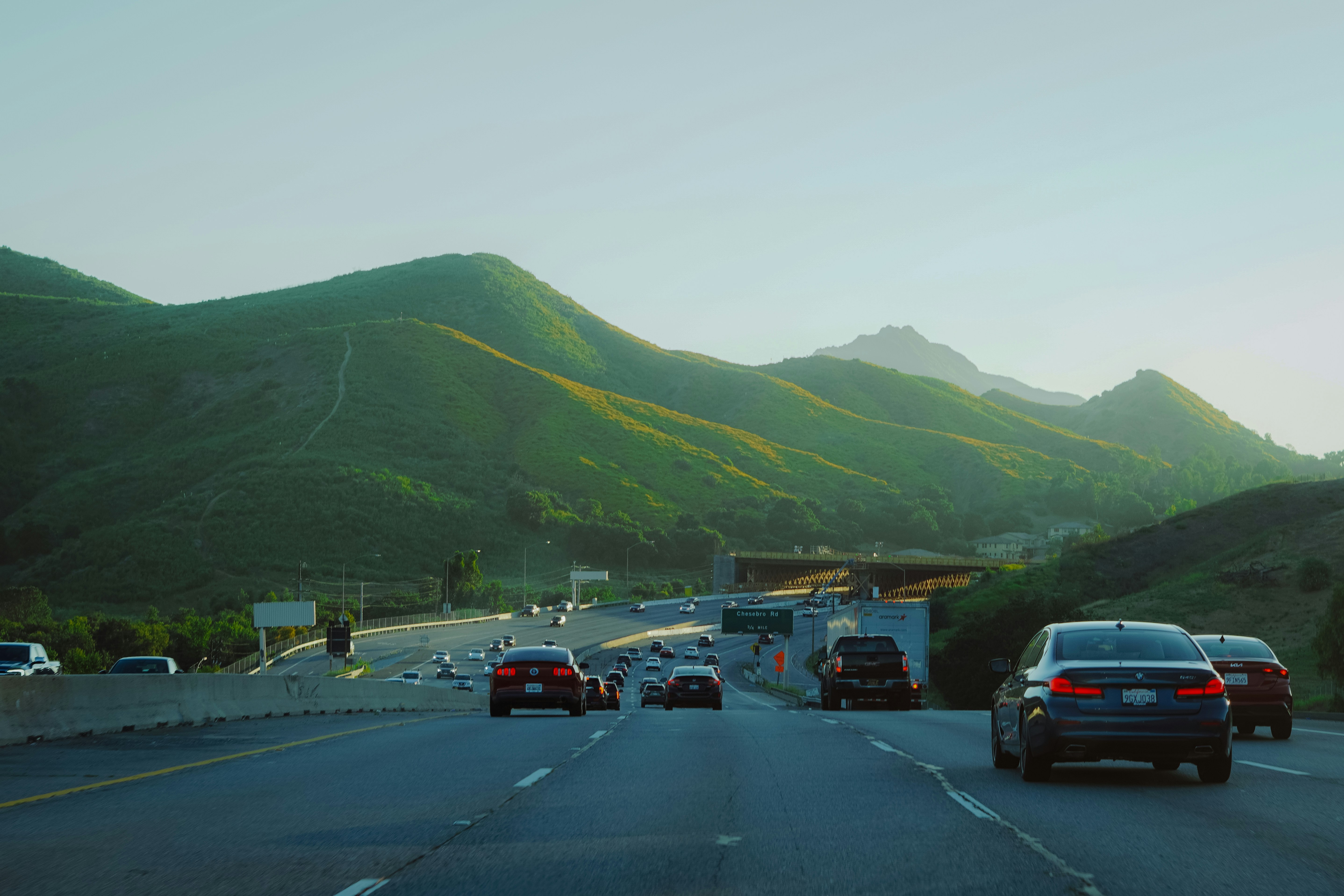 Cars driving on a highway with green mountains.