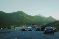 Cars driving on a highway with green mountains.