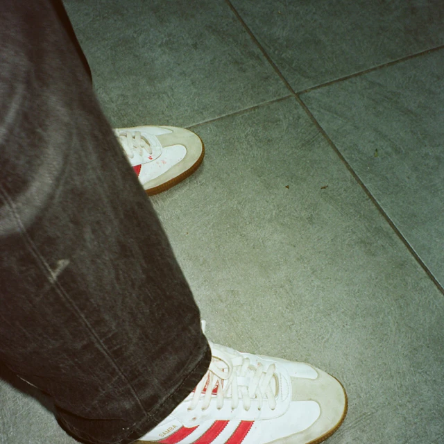 A person wearing low white adidas sneakers with red stripes