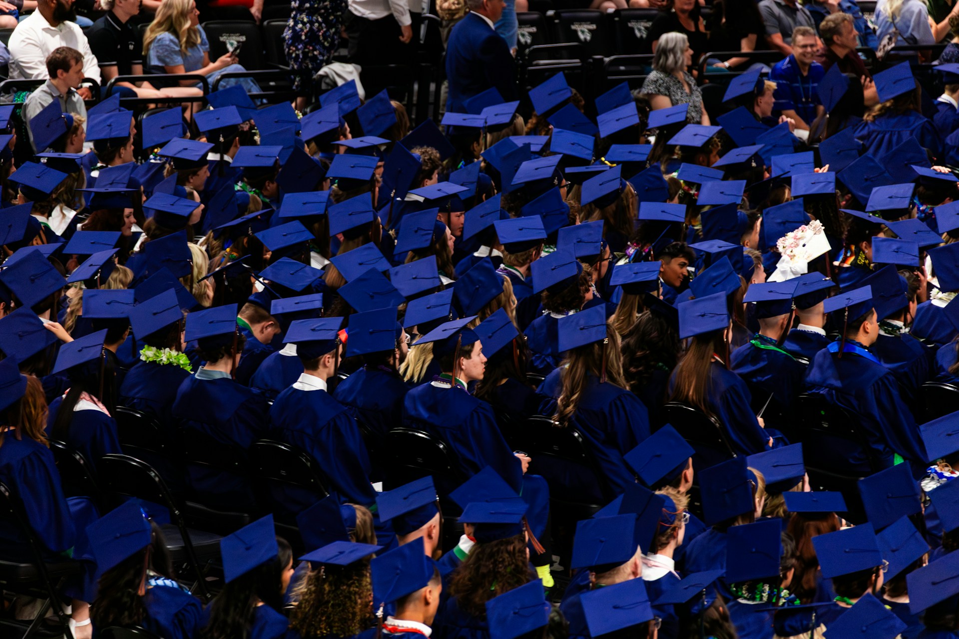 Graduates in blue caps and gowns sit together.