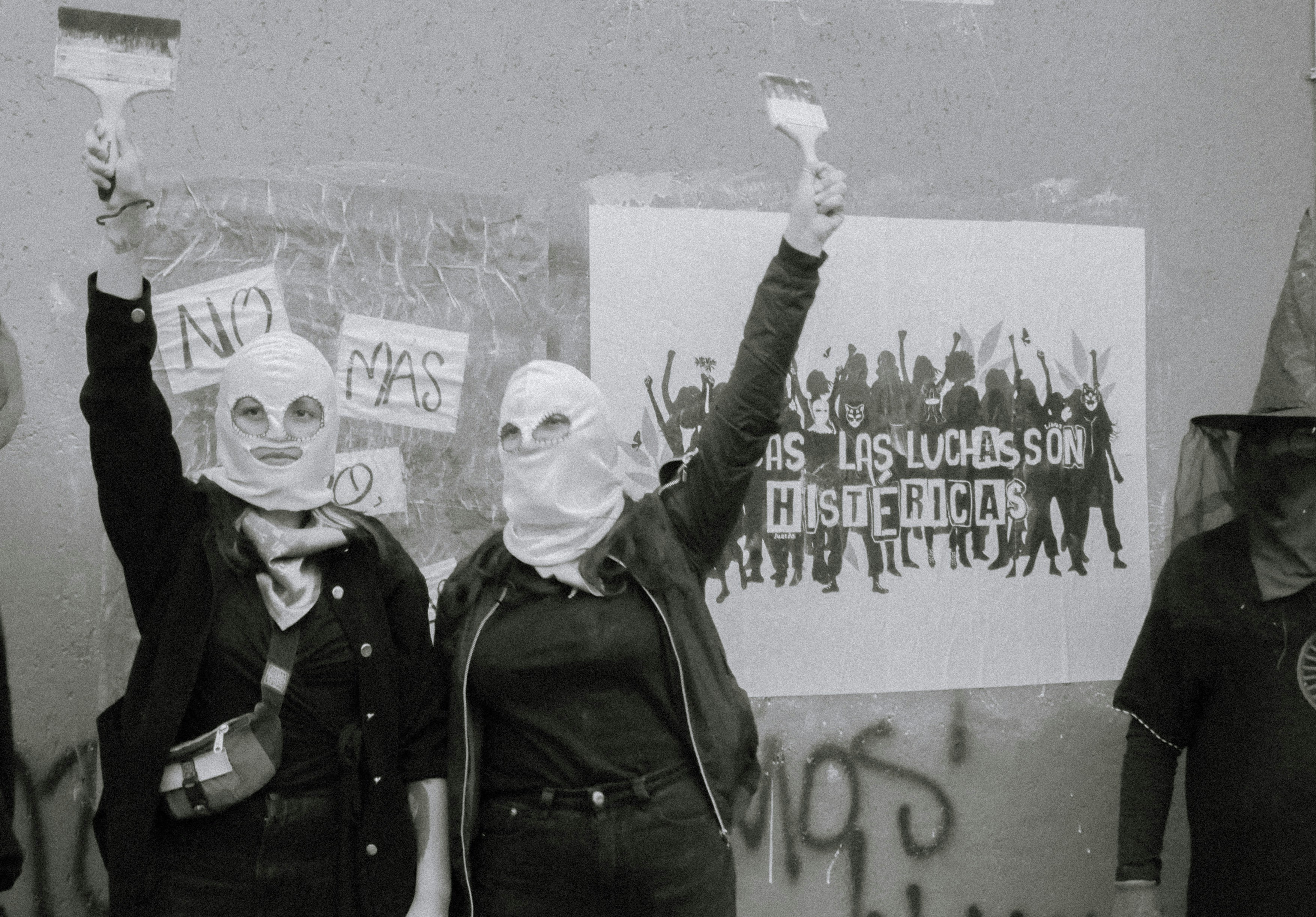 Two women in masks hold paintbrushes aloft.