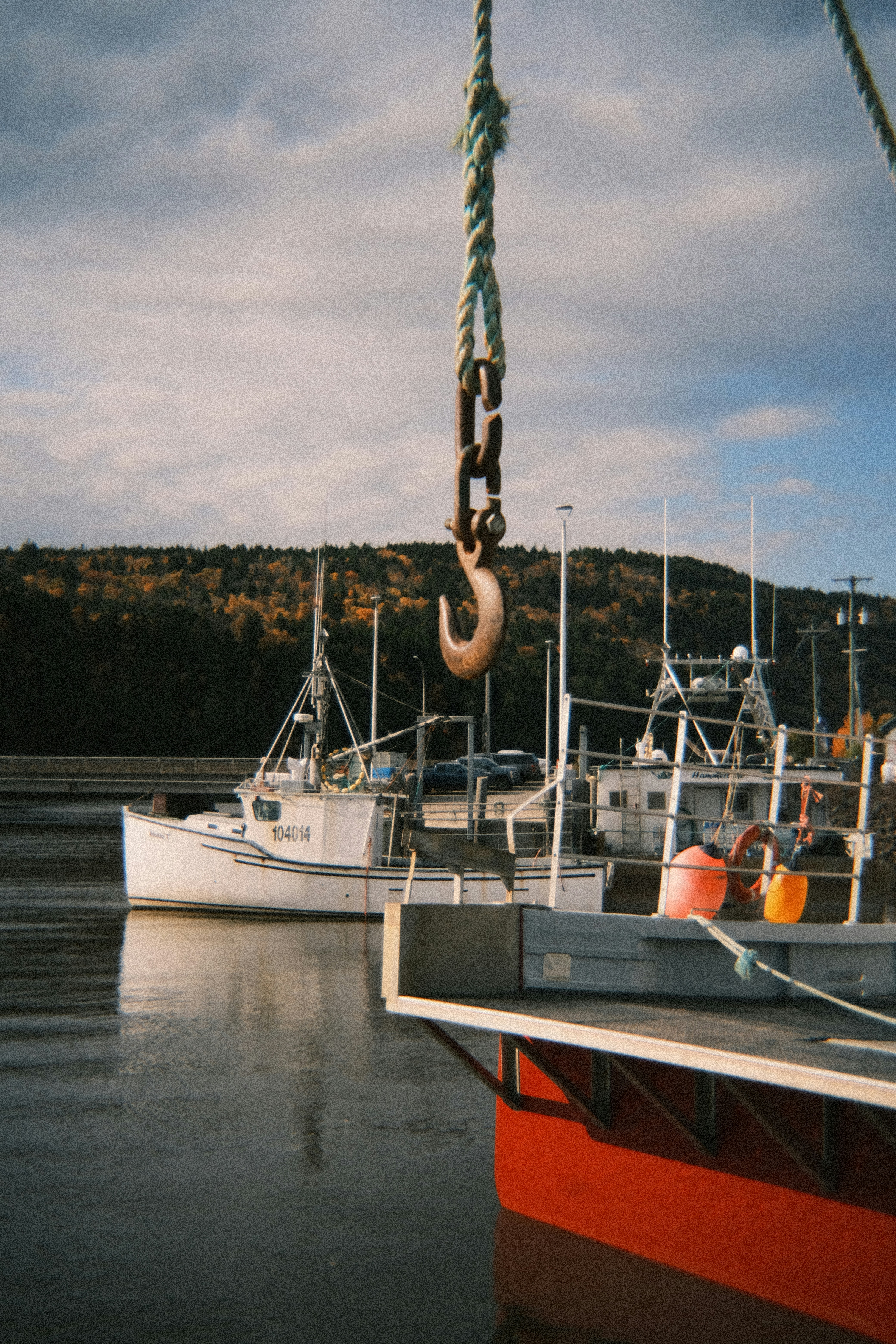 Fishing boats docked at a harbor with a crane hook.