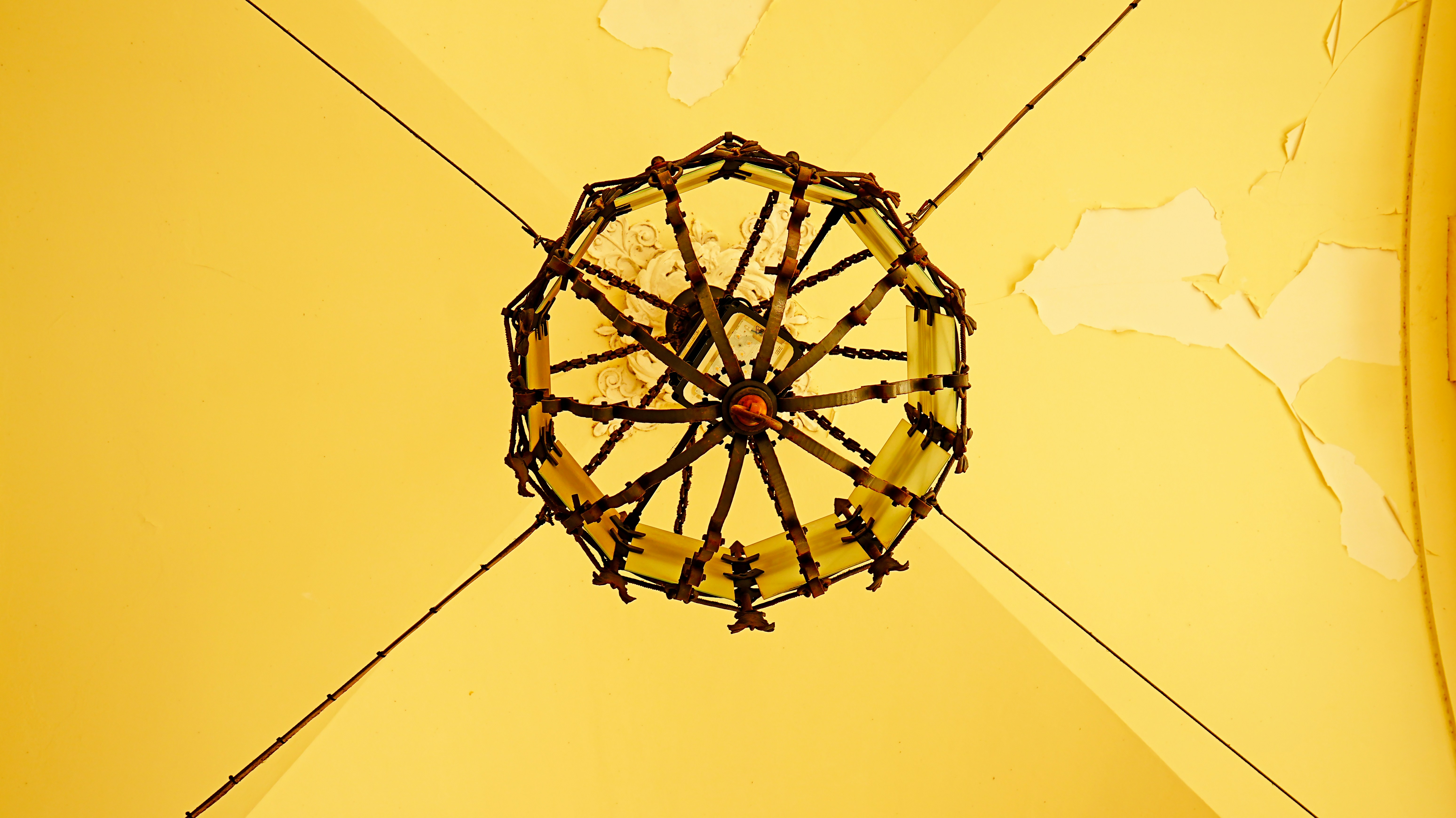 Lámpara de araña ornamentada que cuelga de un techo amarillo.