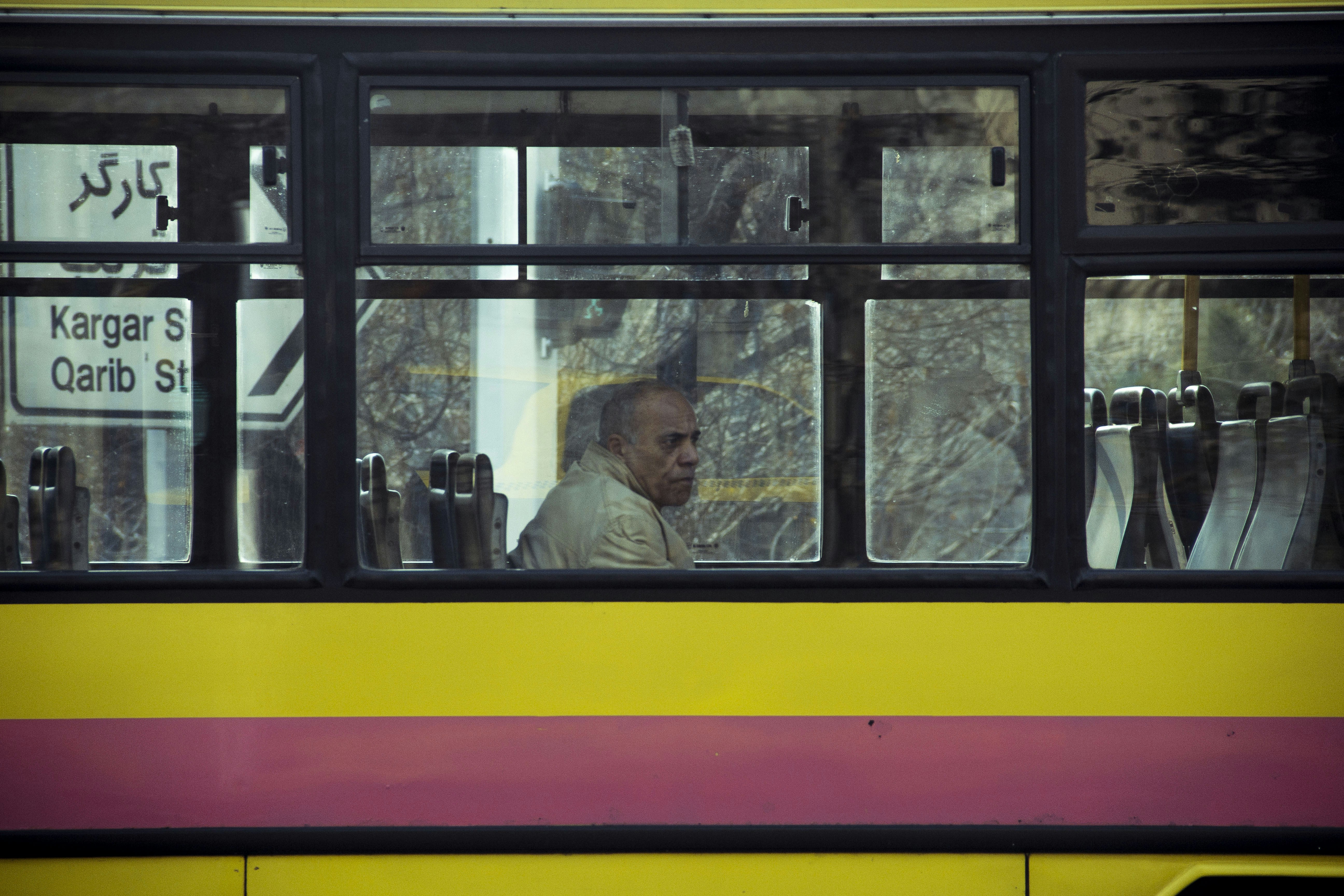 Man sitting inside a yellow and pink bus.