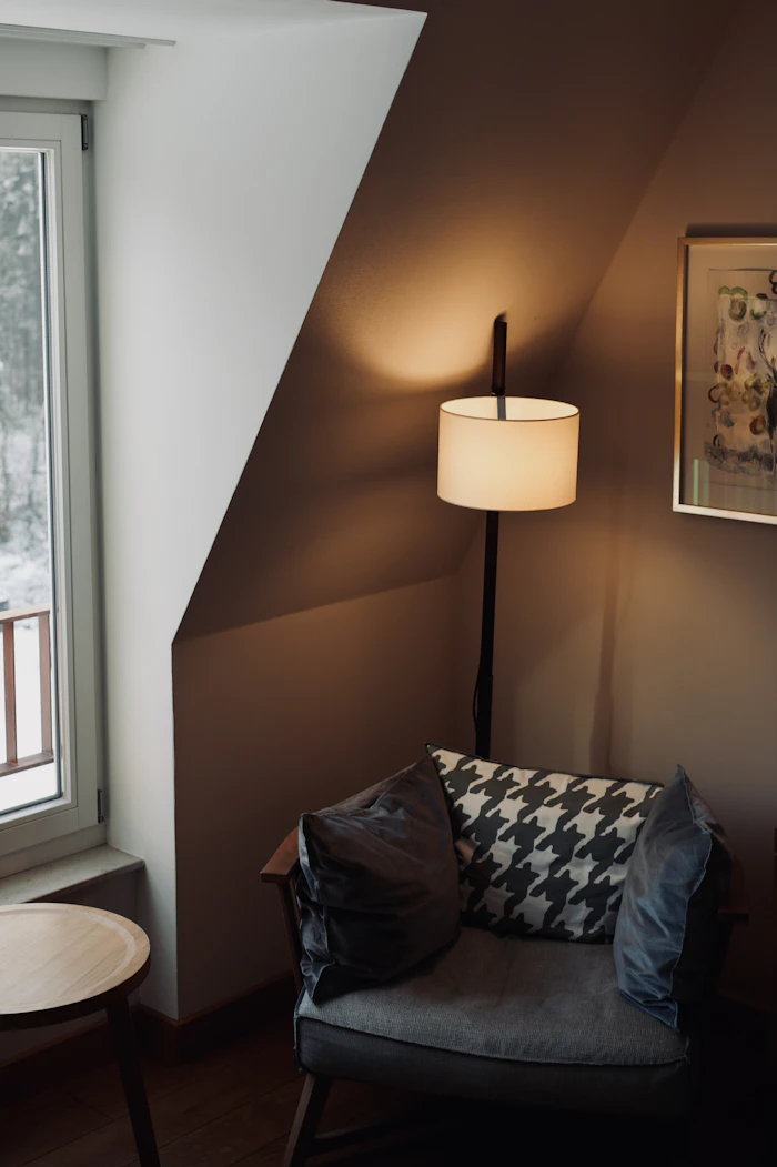 An armchair with a patterned cushion under a glowing floor lamp in a quiet corner