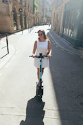 Woman riding an electric scooter down a sunny street.
