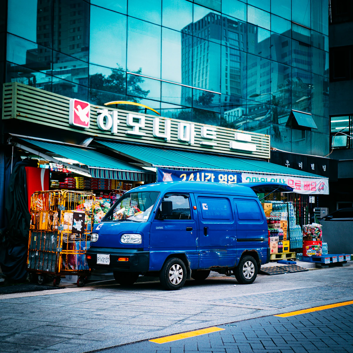Korean neighbourhood mart advertising 24-hour opening with a delivery van outside