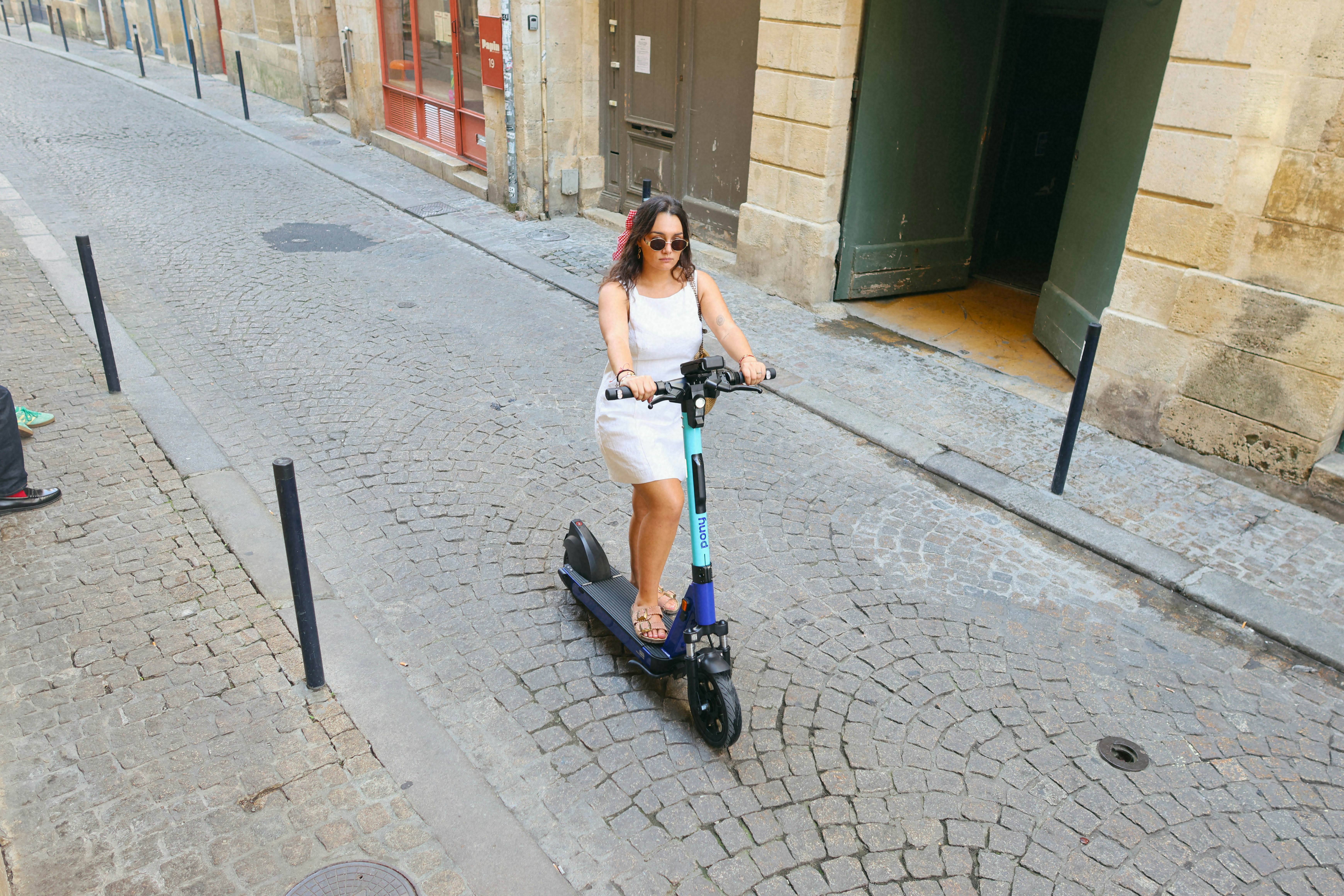 Woman riding an electric scooter down cobblestone street