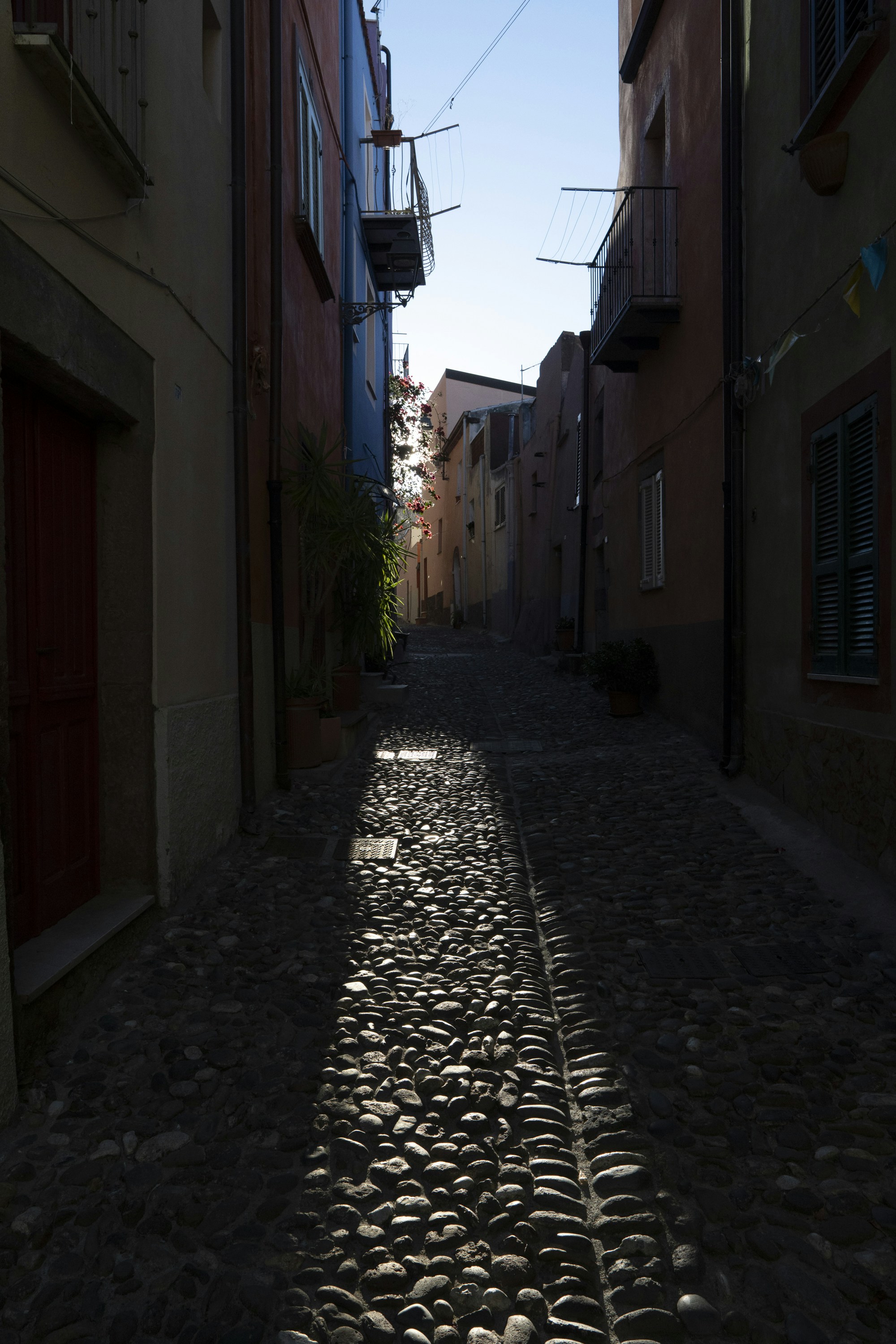 Cobblestone alleyway with colorful buildings and sunlight.