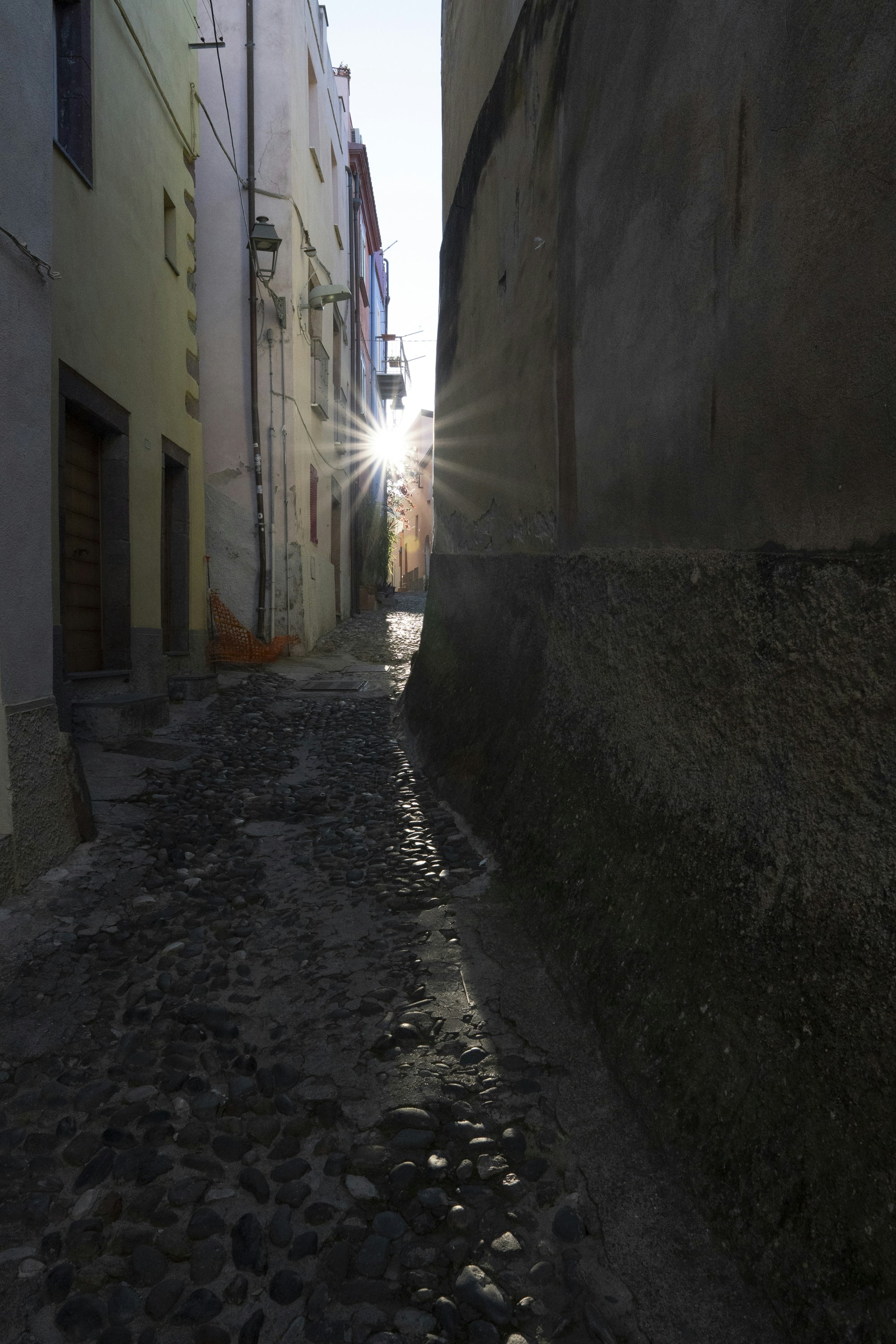 Sunlight streams down a narrow cobblestone alleyway.