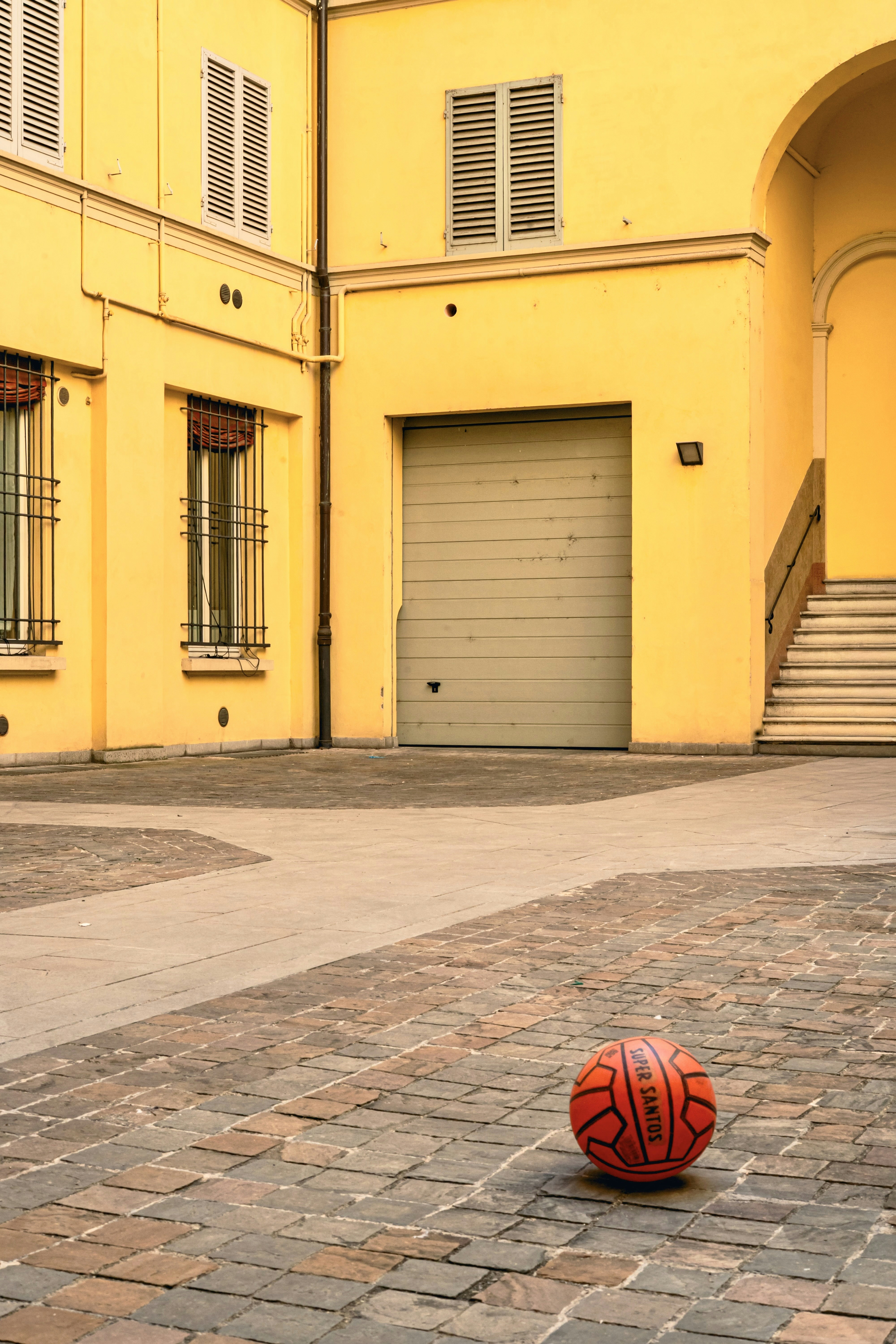 A basketball rests on a cobblestone courtyard.