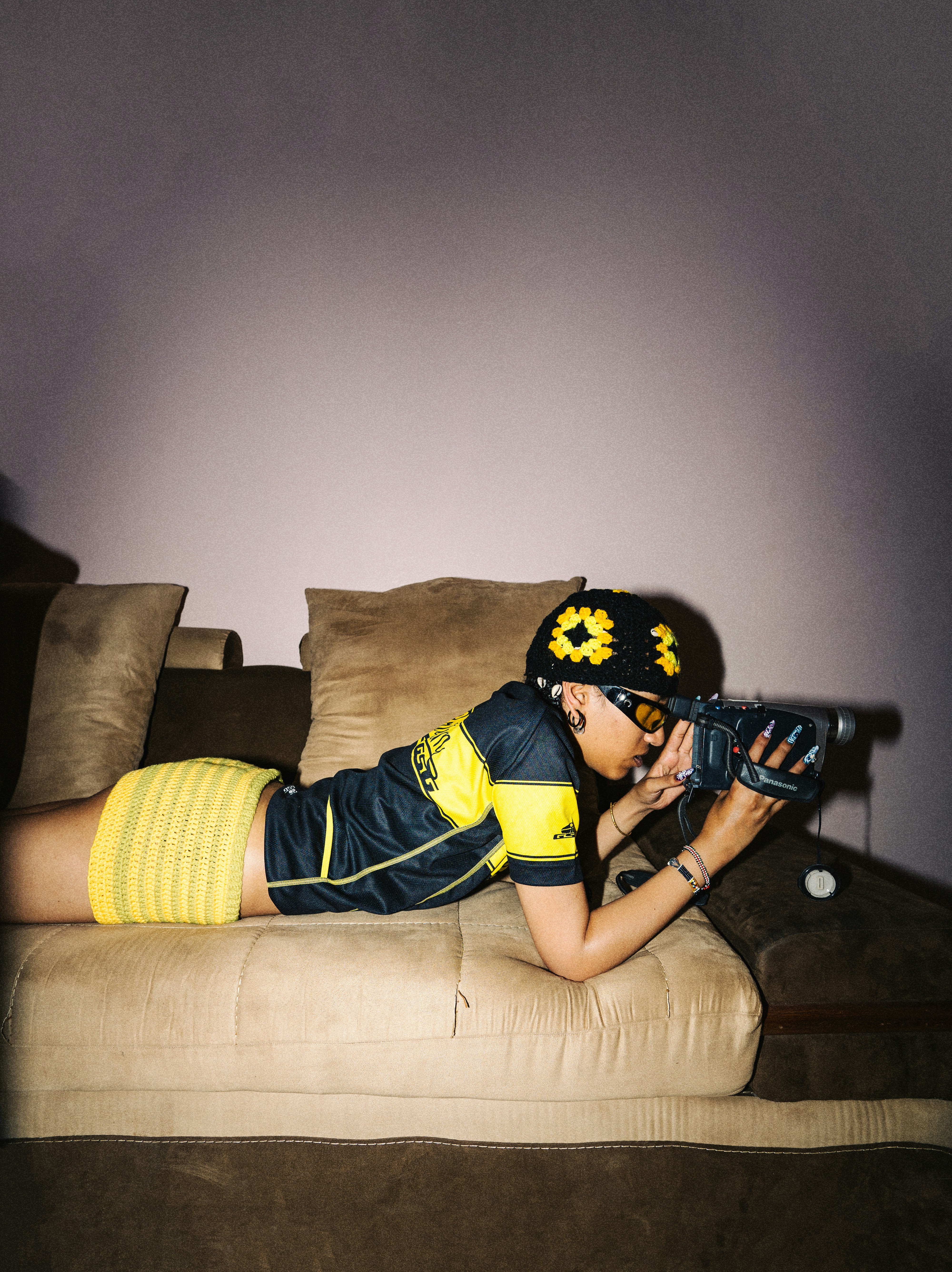 Wanita dengan celana pendek kuning mengarahkan pistol mainan di sofa