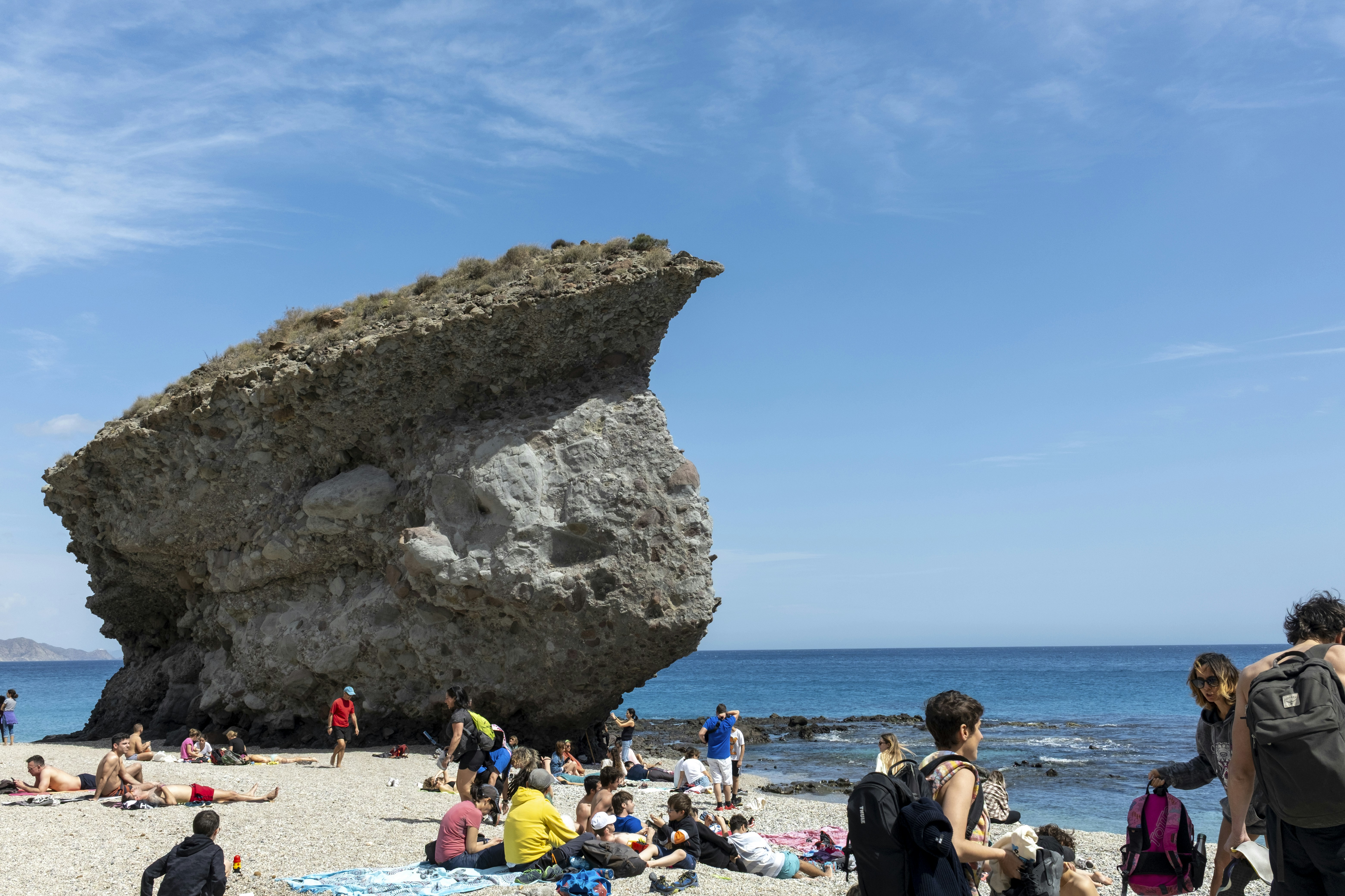 Menschen, die sich an einem sonnigen Strand mit großen Felsformationen entspannen.
