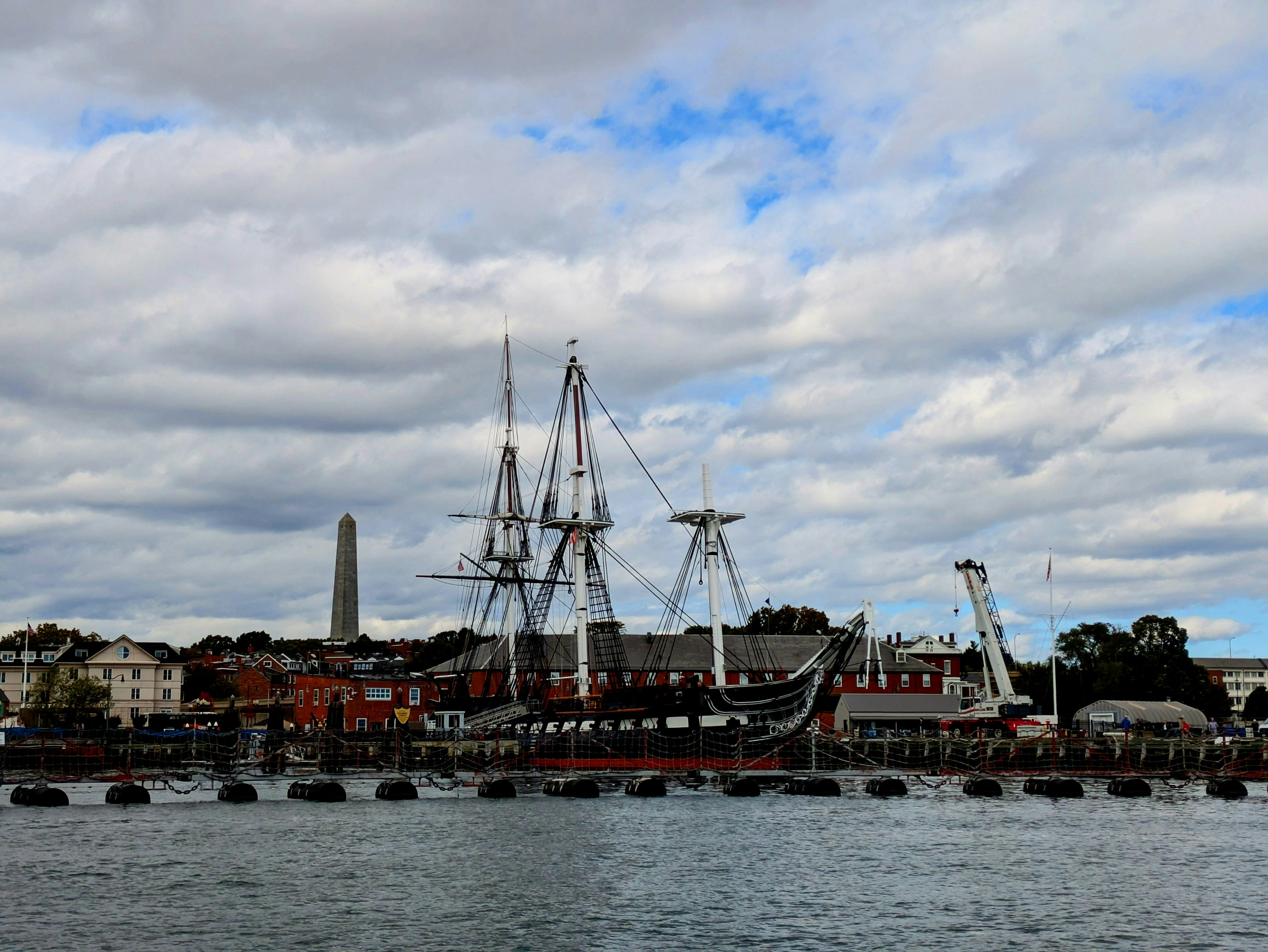 Historic ship docked at a waterfront with monument.