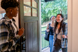 Two women arriving at a doorway, greeted by another woman.