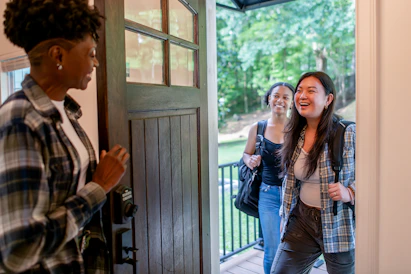 Two women arriving at a doorway, greeted by another woman.