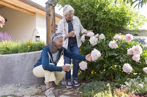 Two women admire pink flowers in a garden.