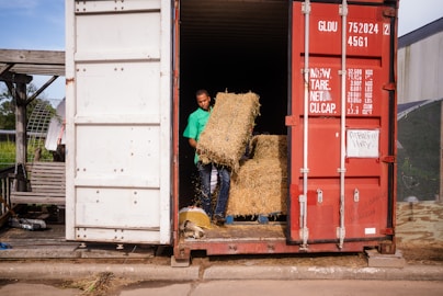 Man loading hay bales into a shipping container.
