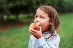A young girl eating a fresh peach outdoors.