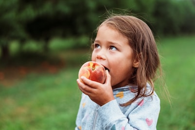 A young girl eating a fresh peach outdoors.