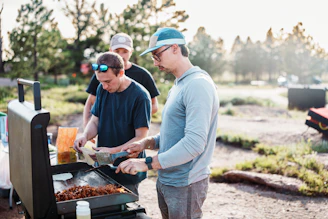 Three men cooking food on an outdoor grill.