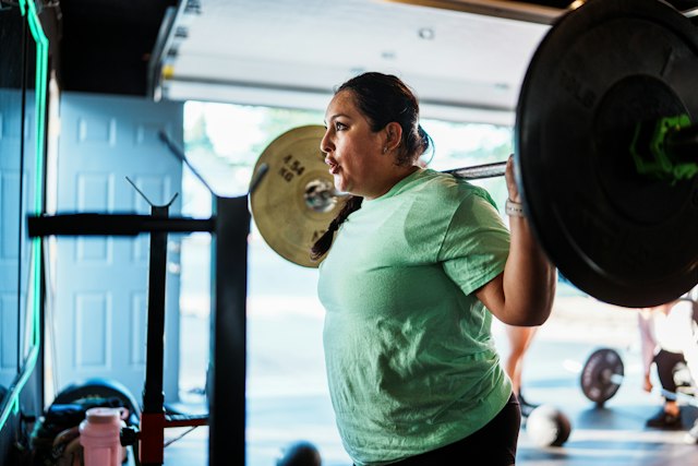 A woman performing a barbell back squat in a bright garage gym