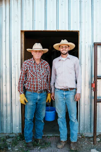 Two farmers wearing straw hats stand in a doorway