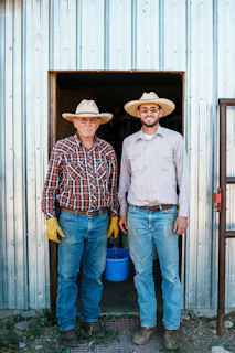 Two farmers wearing straw hats stand in a doorway