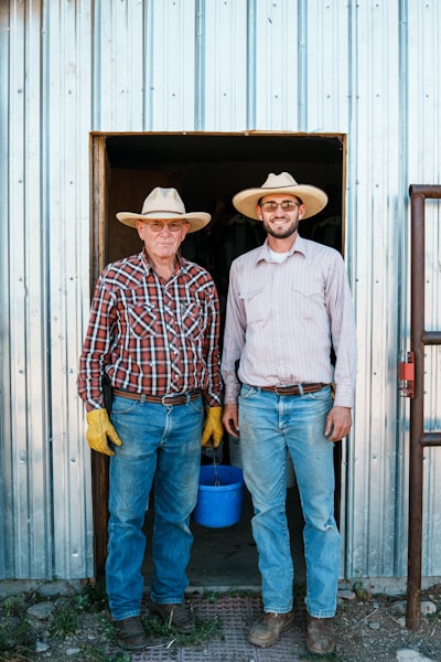 Two farmers wearing straw hats stand in a doorway.