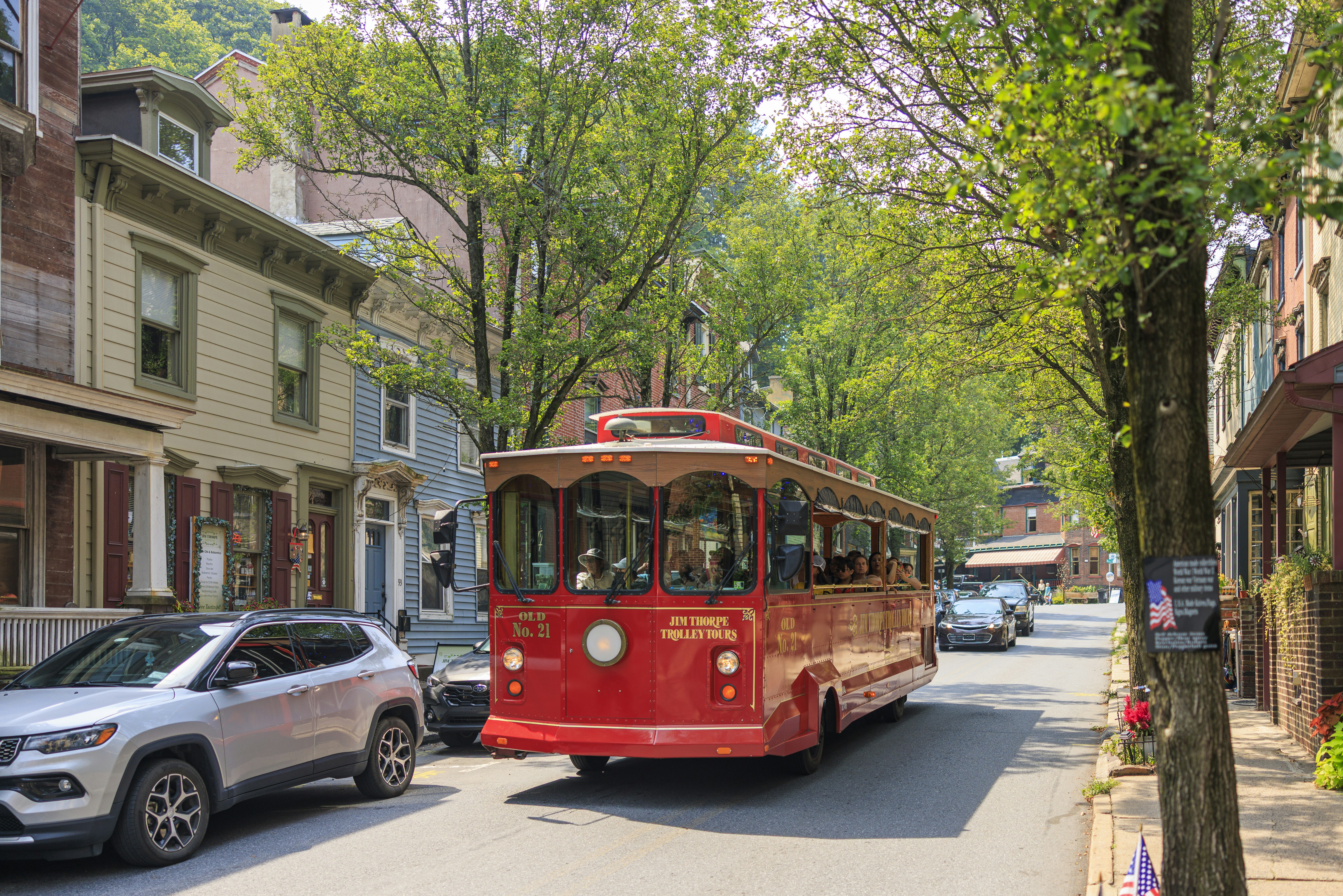 Red trolley car driving down a tree-lined street.