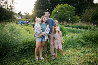 Family standing in a lush green field with tractor