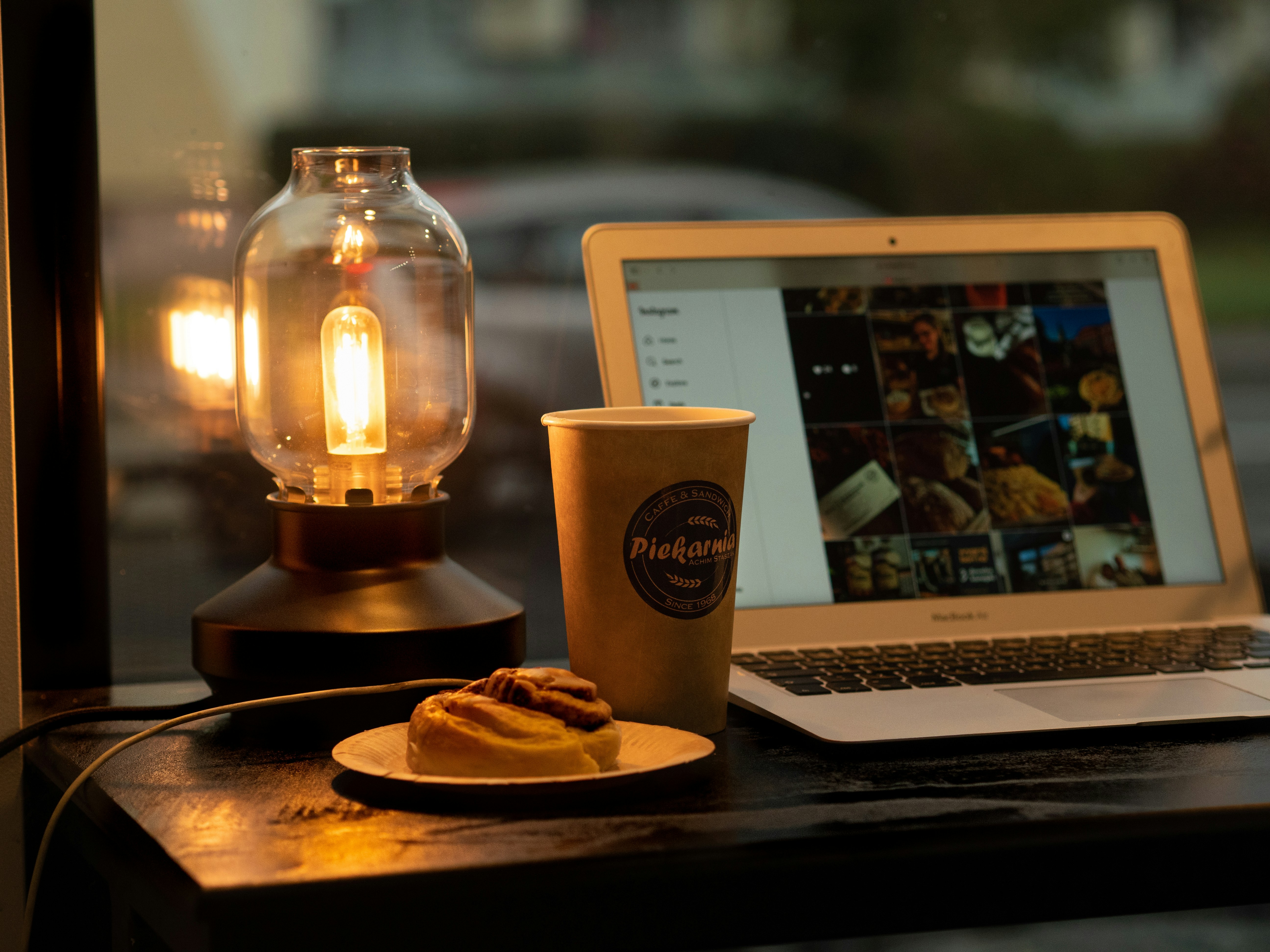 Laptop, coffee, and pastry by a vintage lamp.