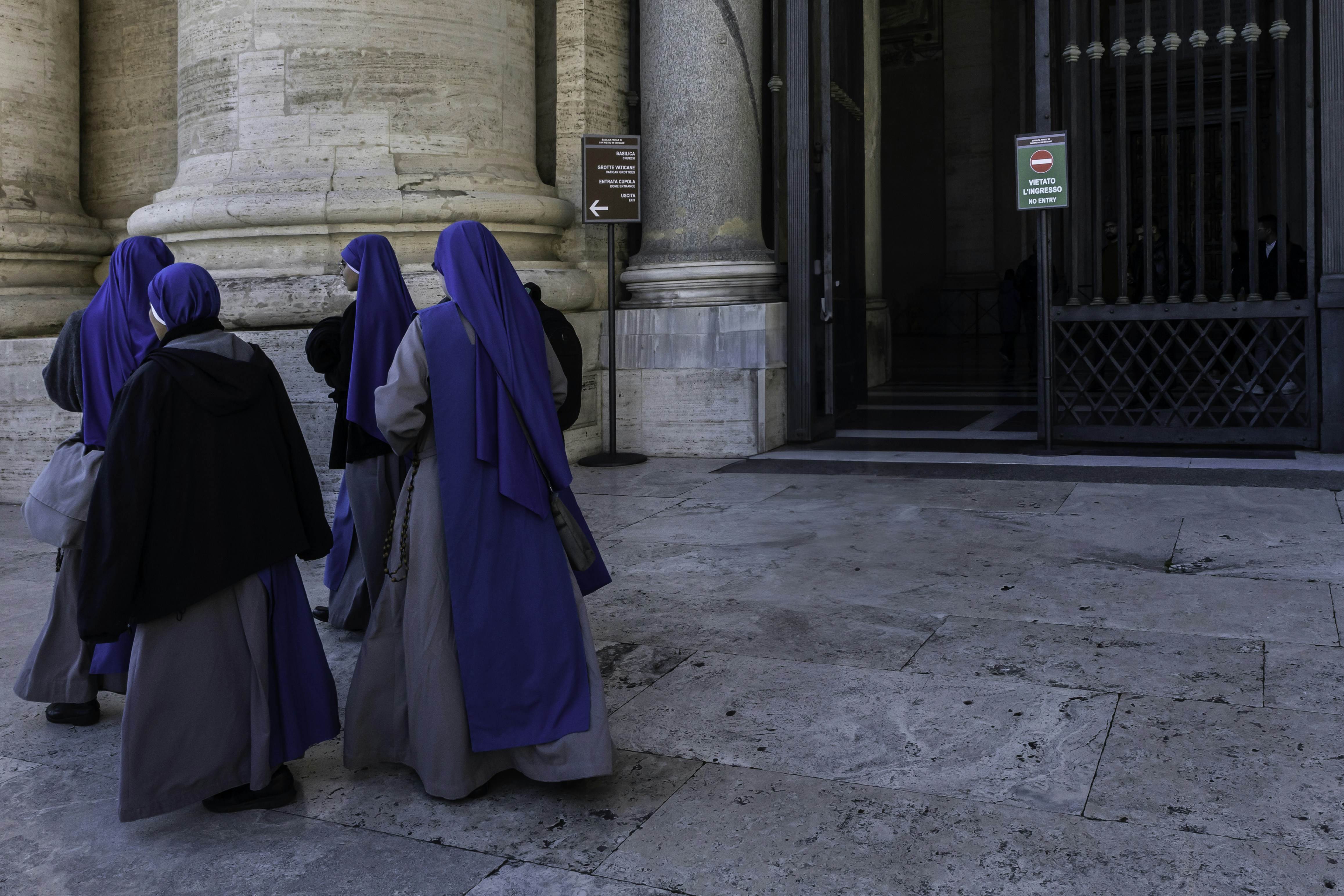 Nuns in blue habits walking near a building entrance.
