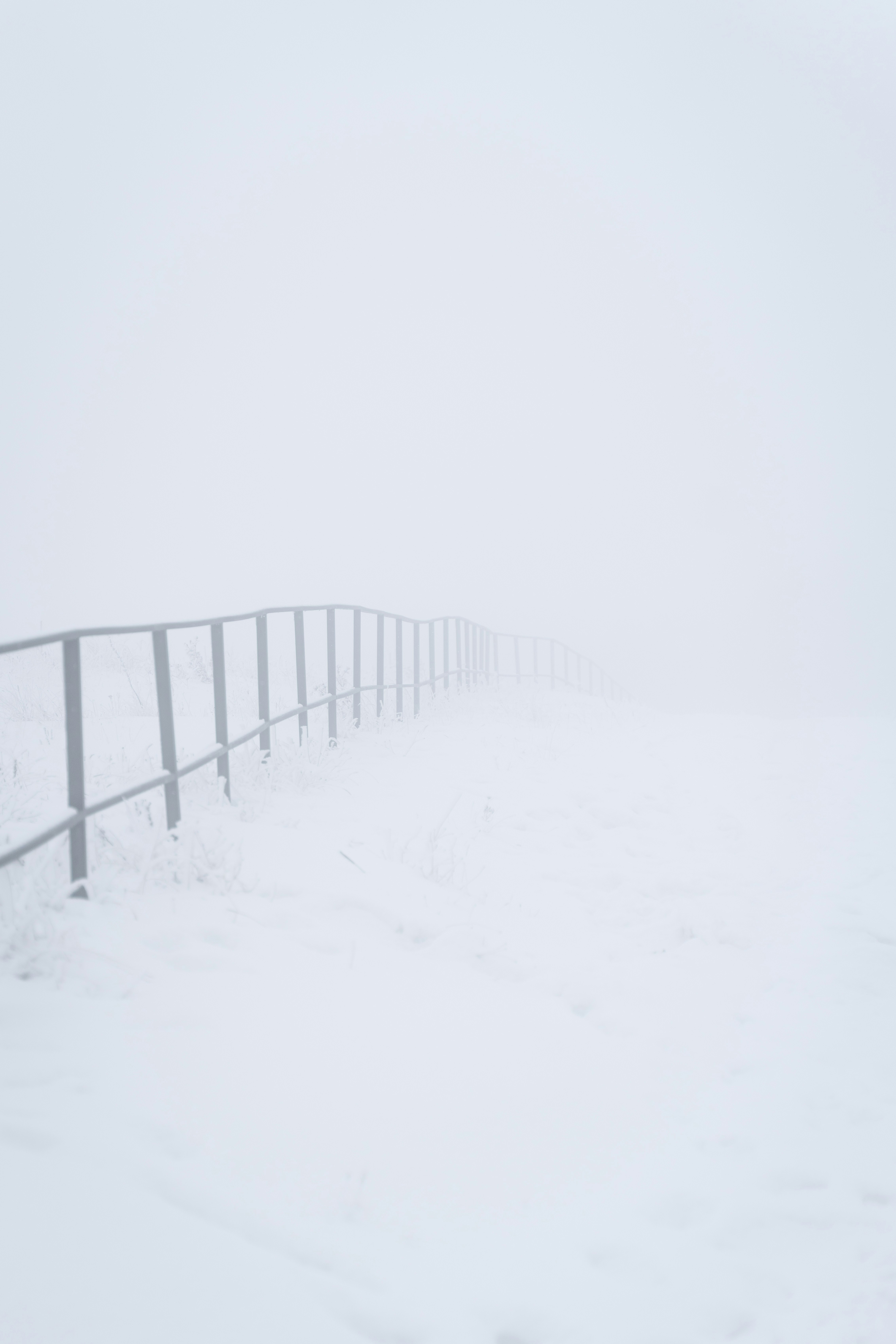 A metal railing in a snowy landscape with fog