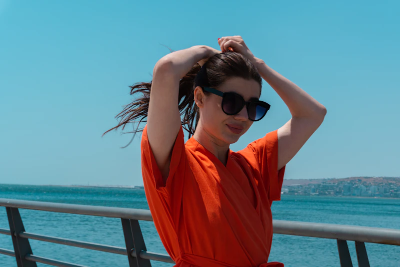 femme en robe orange attachant ses cheveux face à l’océan