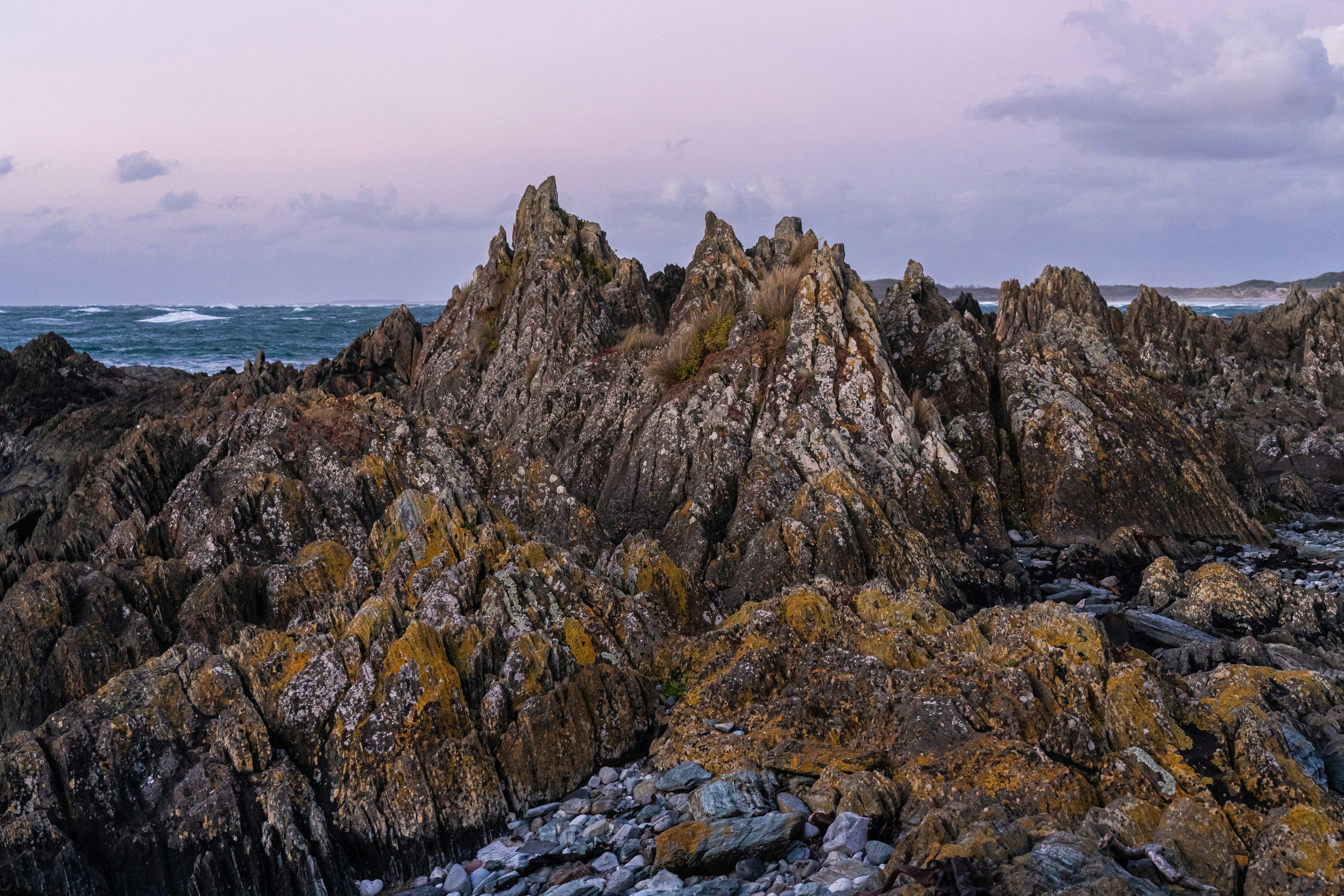 Jagged rocky coastline at dusk with pastel sky