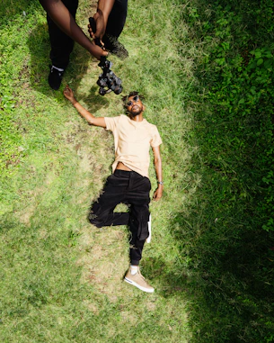 Man lying on grass while someone films him.