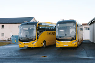 Two yellow tour buses parked outside buildings