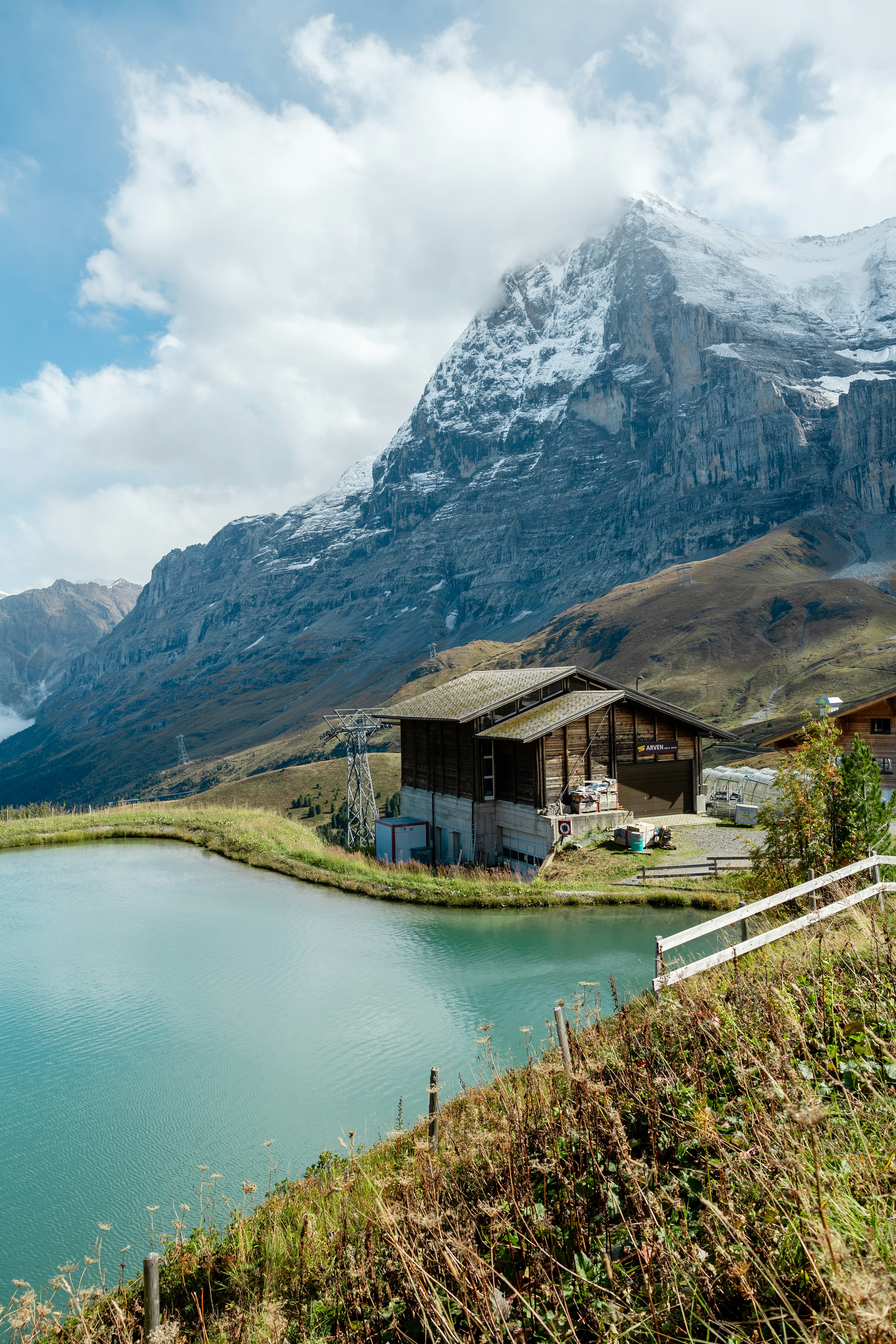 Alpine lake with wooden buildings and snowy mountain.