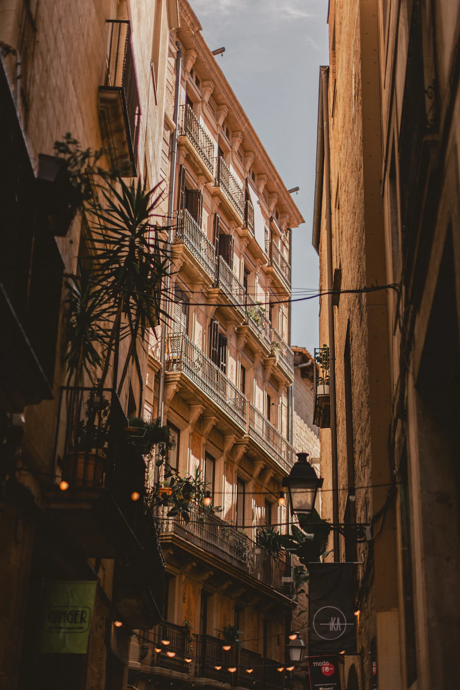 Carrer estret de Gracia al capvespre, amb balcons plens de plantes, fanals i façanes de tons terracota.