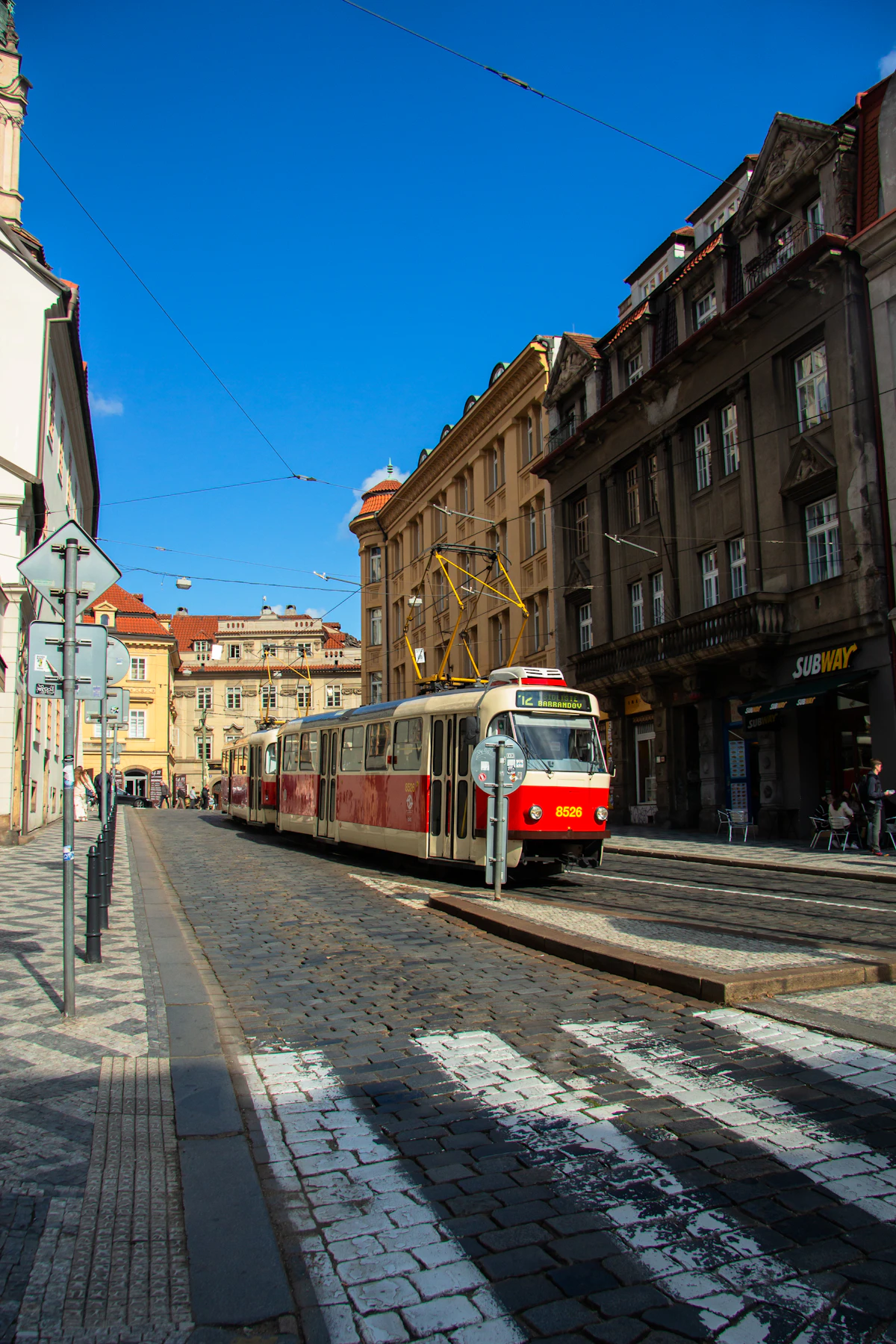 Red and cream Prague tram on cobblestone tracks with Old Town church spires in the background