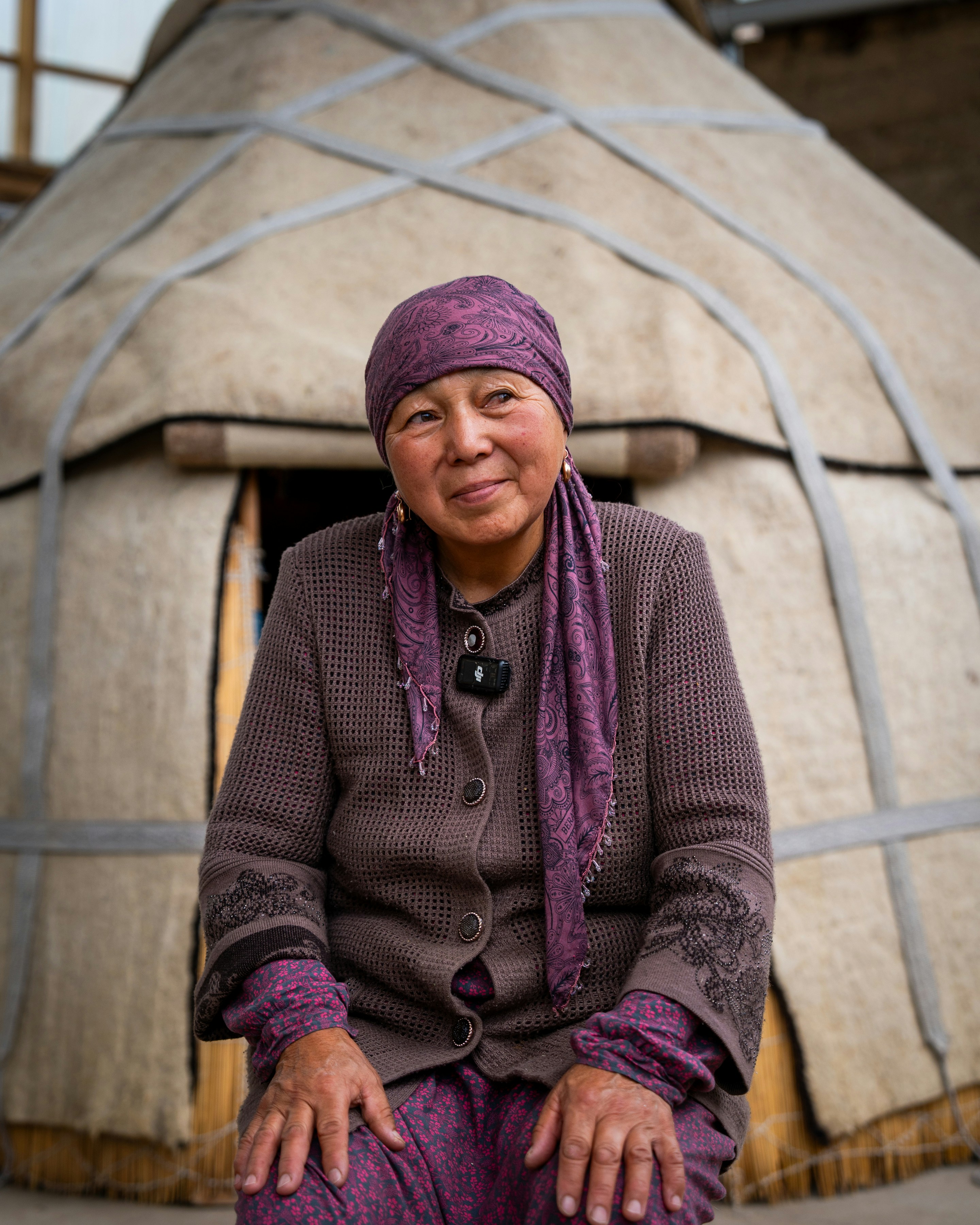 Elderly woman in traditional clothing sits outside yurt