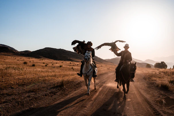 Two people on horseback with eagles at sunset