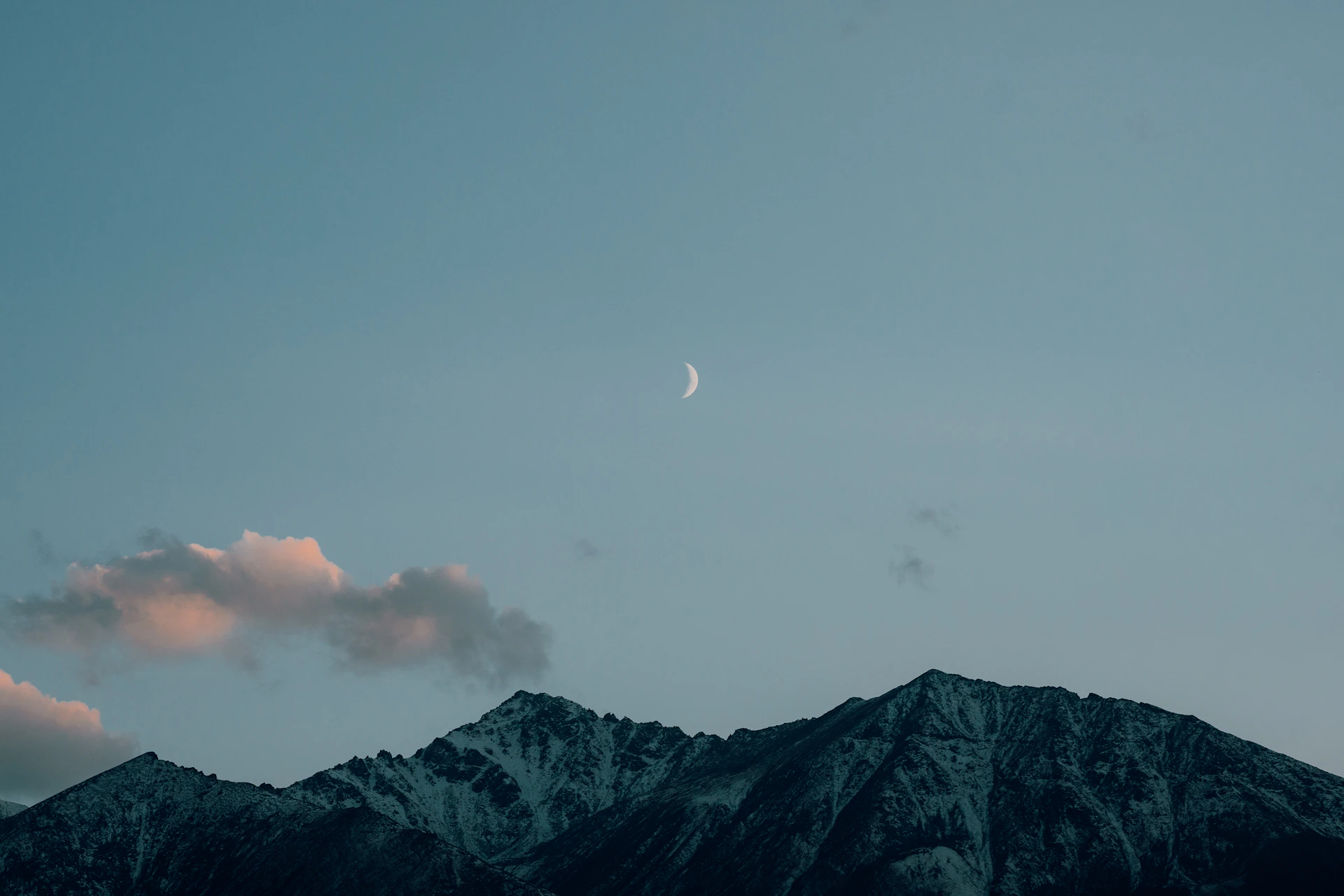 Crescent moon above snow-capped mountains at dusk